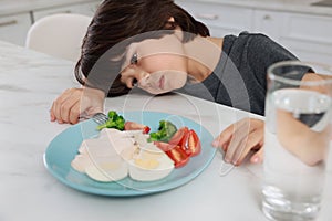 Cute little boy refusing to eat dinner in kitchen