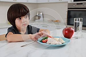 Cute little boy refusing to eat dinner in kitchen