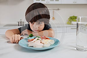 Cute little boy refusing to eat dinner in kitchen