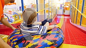 Cute little boy riding down the slide on inflatable donut ring in child`s playing room at shopping mall