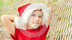 Cute little boy in Santa hat dreaming about christmas gifts. Christmas family vacation, travel, trip. Happy child lying in hammock