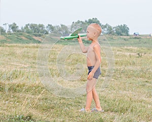 Cute little boy in shorts walks across the field and holds a toy airplane in his hand