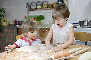 Cute Little Boy Showing His Twin Brother How to Flatten Dough at the Kitchen Table photo