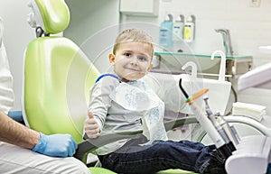 Cute little boy showing thumb up sign at dentist`s office clini