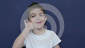 Cute little boy shows thumbs up gesture, happy facial expression emotion, slow motion isolated on blue background