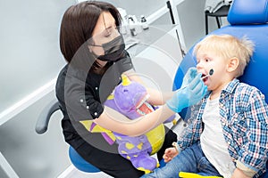 A cute little boy sits at the dentist, opened his mouth, showing his teeth to the dentist. Happy boy is sitting in