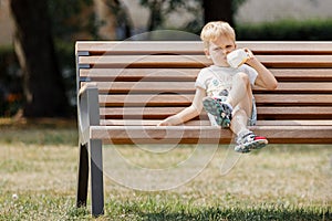 Cute little boy sitting on a bench and drinks juice