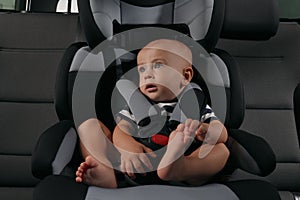 Cute little boy sitting in child safety seat inside car