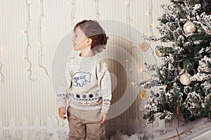 Cute little boy is sitting with a gift near the Christmas tree. The child is happy with New Year`s gift. Caucasian
