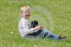 Cute little boy sitting in the grass with his baseball glove