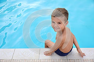 Cute little boy sitting near swimming pool