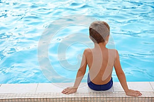 Cute little boy sitting near swimming pool