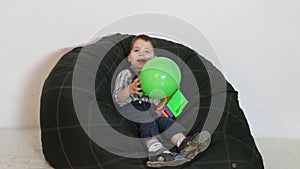 Cute little boy sitting on soft bag with ball