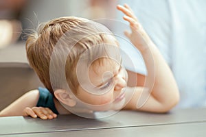 Cute little boy sitting at a table in a park is very upset photo