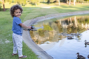 Cute little boy smiling as he learns to fish in a pond at an outdoor park.