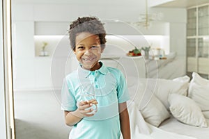 Cute little boy smiling and drinking water from glass on white background