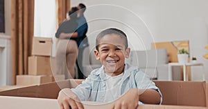 A cute little boy smiling sits in a cardboard box used for packing things during a move the child looks at his parents