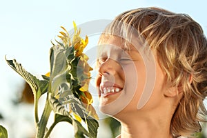 Cute little boy sniffing sunflower outdoors. Child spending time in nature