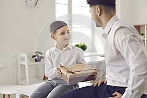 Cute little boy son gives dad a gift in a gift box in honor of his father& x27;s day or birthday.