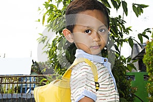 Cute little boy standing looking sideways wearing yellow school bag