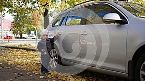 Cute little boy standing near the grey car on a city street in autumn