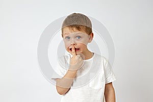 Cute little boy standing on a white background and putting his index finger to his lips