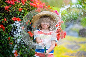 Cute little boy in straw hat is laughing with water spraying hose.