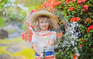 Cute little boy in straw hat is laughing with water spraying hose.