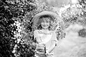 Cute little boy in straw hat is laughing with water spraying hose.