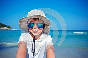 Cute little boy in sunglasses making selfie at tropical beach on exotic island