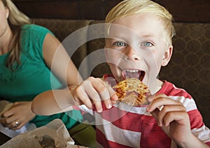 Cute little boy taking a big bite of cheese pizza at a restaurant