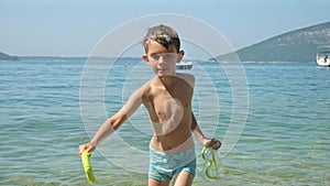 Cute little boy taking off diving mask after swimming in sea and walking out on the beach