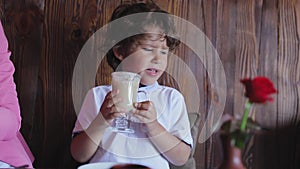 Cute little boy tasting coffee from cup at cafe
