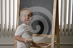 Cute little boy toddler, two years old. Drawing on the chalkbo
