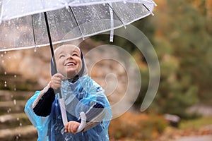 Cute little boy with transparent umbrella under rain outdoors