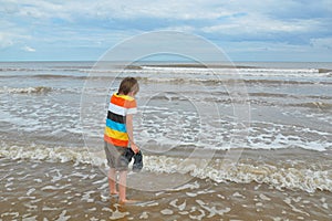 Cute little boy tries cold water in waves on beach