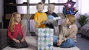 Cute little boy unwrapping gift box with present