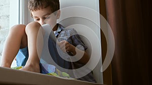 Cute little boy uses a white tablet PC on a windowsill at home