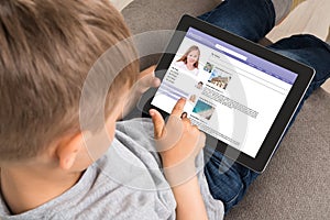 Cute Little Boy Using Social Networking Site On Digital Tablet