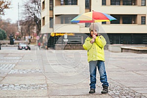 Cute little boy walking in city with colorful rainbow umbrella during rainy autumn day. Cold rainy weather