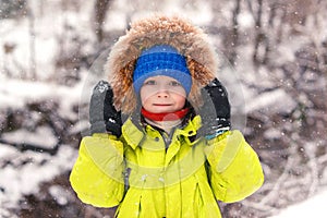 Cute little boy walking under the snow. Happy smiling boy in winter clothes. Snowy winter weather. Beautiful winter park. Kid