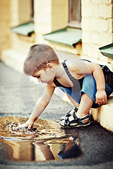 Cute little boy washing hands in puddle