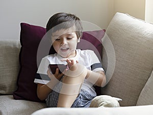 Cute little boy watching cartoons on mobile phone,Preschool kid sititng on sofa with smiling face playing games on smart phone,