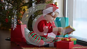 Cute little boy wearing Santa hat opening a Christmas gift. Happy kid on Christmas morning.