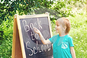 Cute little boy writting on blackboard outdoor . Back to school concept.