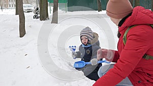 Cute little boy and young mother play in the winter with snow in the park. Blue kid`s jacket and red at mom.