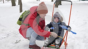 Cute little boy and young mother play in the winter with snow in the park. Blue kid`s jacket and red at mom.