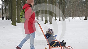 Cute little boy and young mother play in the winter with snow in the park. Blue kid`s jacket and red at mom.