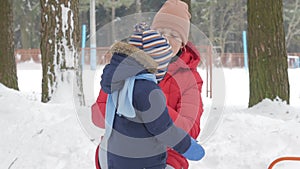 Cute little boy and young mother play in the winter with snow in the park. Blue kid`s jacket and red at mom.