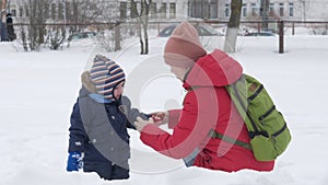 Cute little boy and young mother play in the winter with snow in the park. Blue kid`s jacket and red at mom.